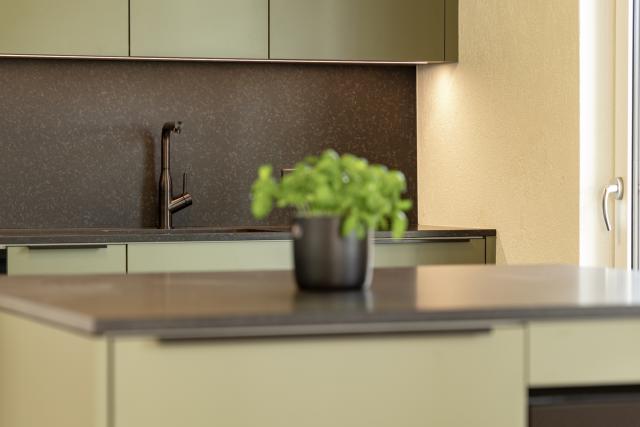 Kellenberger AG Schreinerei - Küche mit olivefarbenen Fronten, schwarzer Granitabdeckung und schwarzen Armaturen