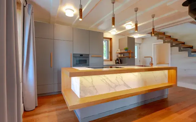 Kücheninsel mit Keramik Arbeitsfläche und beleuchtetem Vorbau aus Kirschbaum.