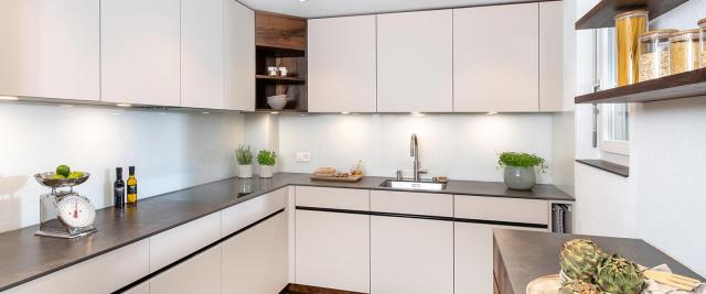 Moderne Küche in Weiss mit dunklen Altholzdetails, grifflosen Fronten und klarer L-Form mit grosszügiger Arbeitsfläche