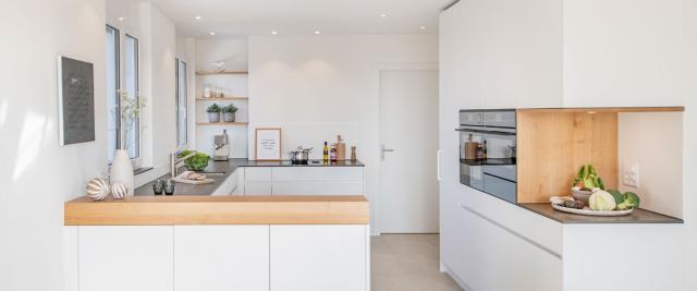 Moderne, helle Designküche in Weiss mit warmen Holzakzenten, grifflosen Fronten und klarer Linienführung in U-Form.