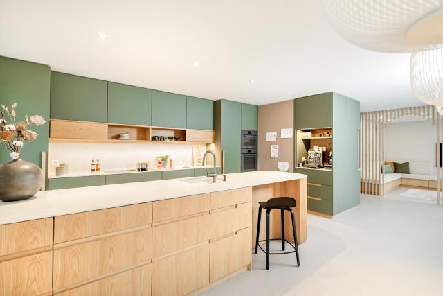 Helle, nachhaltige Küche mit grünen Linoleumfronten, warmem Eichenfurnier und einer hellen, robusten Arbeitsfläche aus Dekton im minimalistischen Design